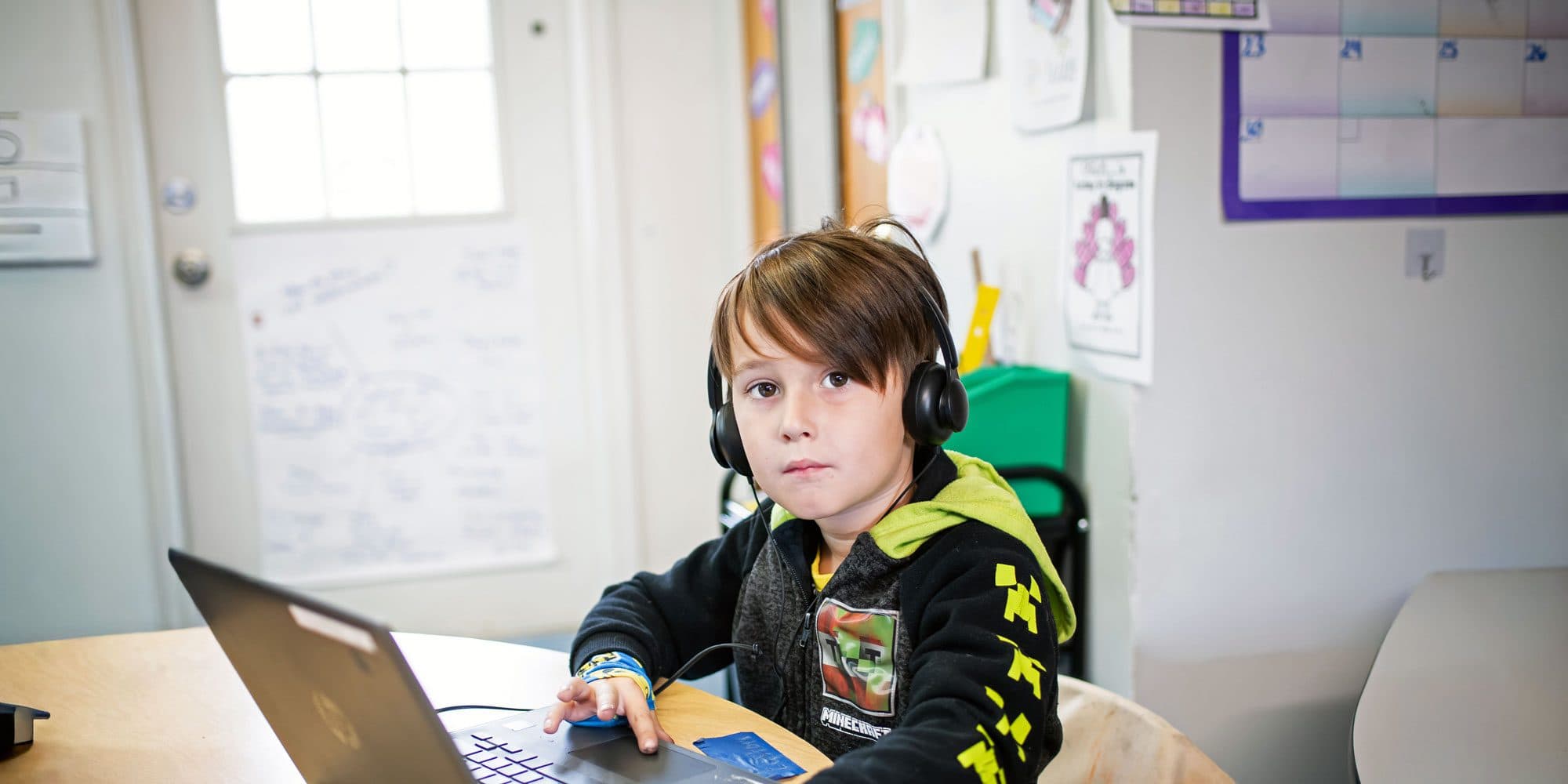Student wearing headphones working on a laptop in a classroom.