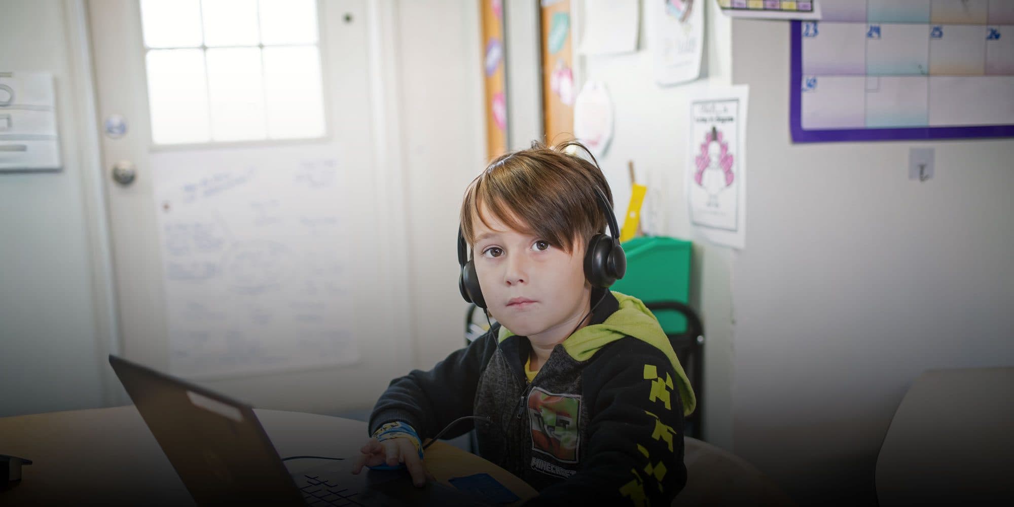 Student wearing headphones working on a laptop in a classroom.