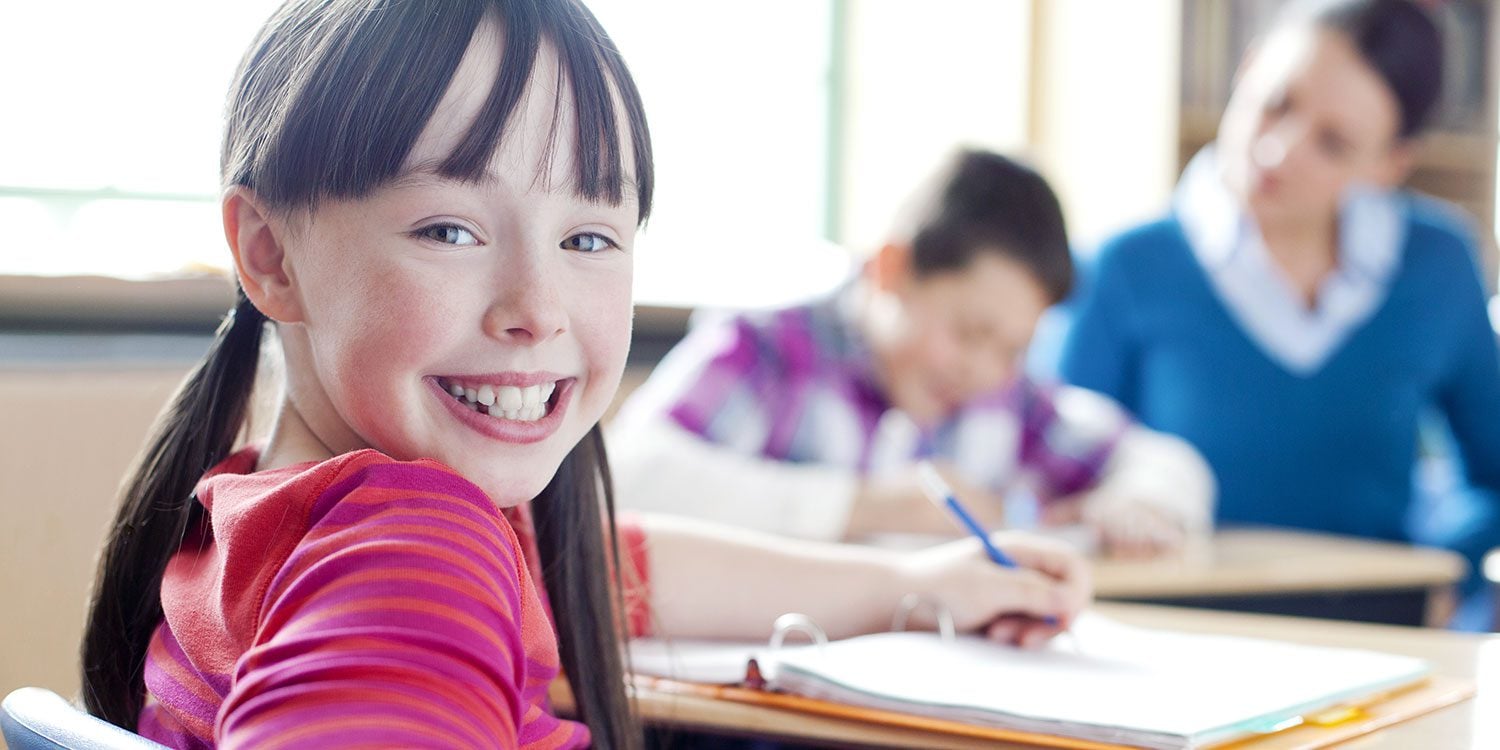 Smiling child in classroom with other students and adult.