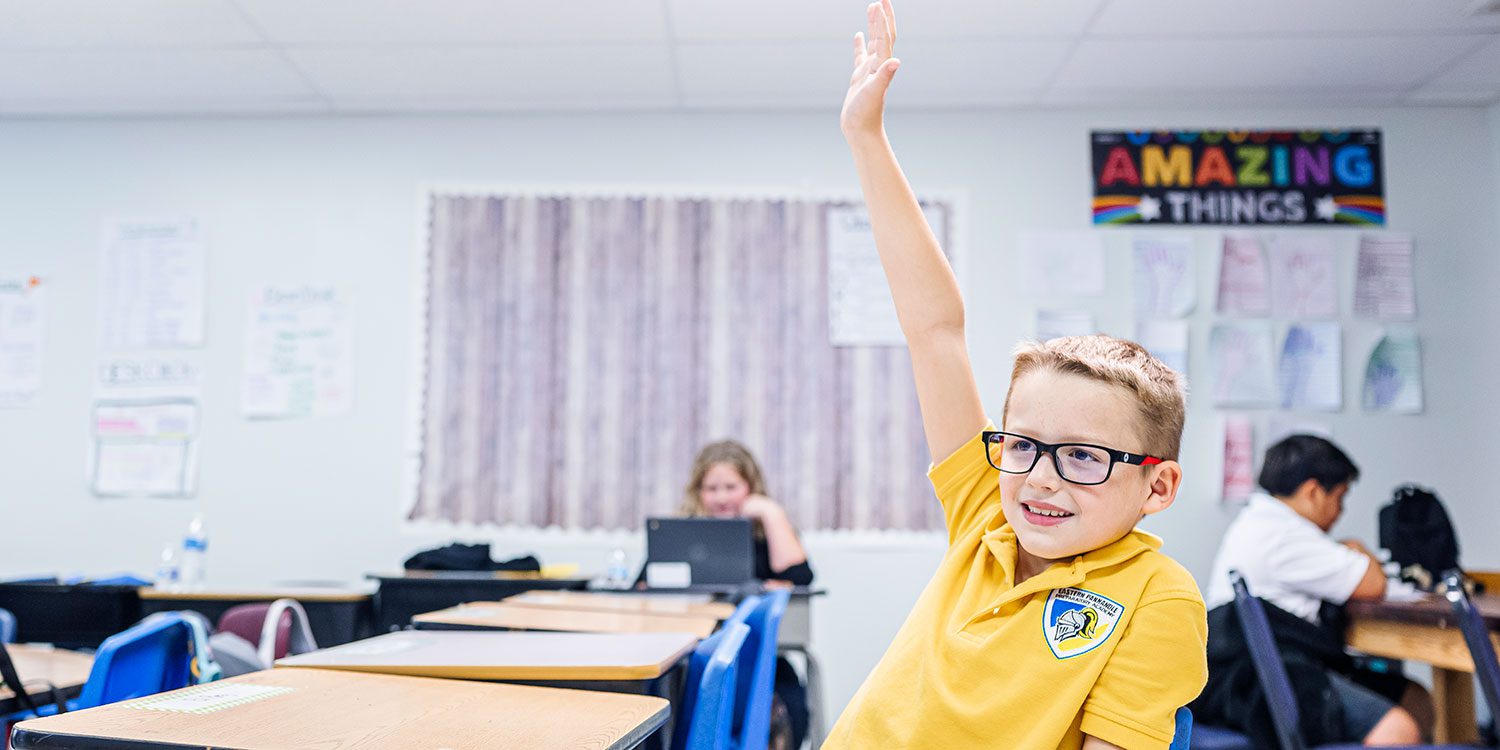 Smiling student in an EPPA uniform shirt raising a hand in class.