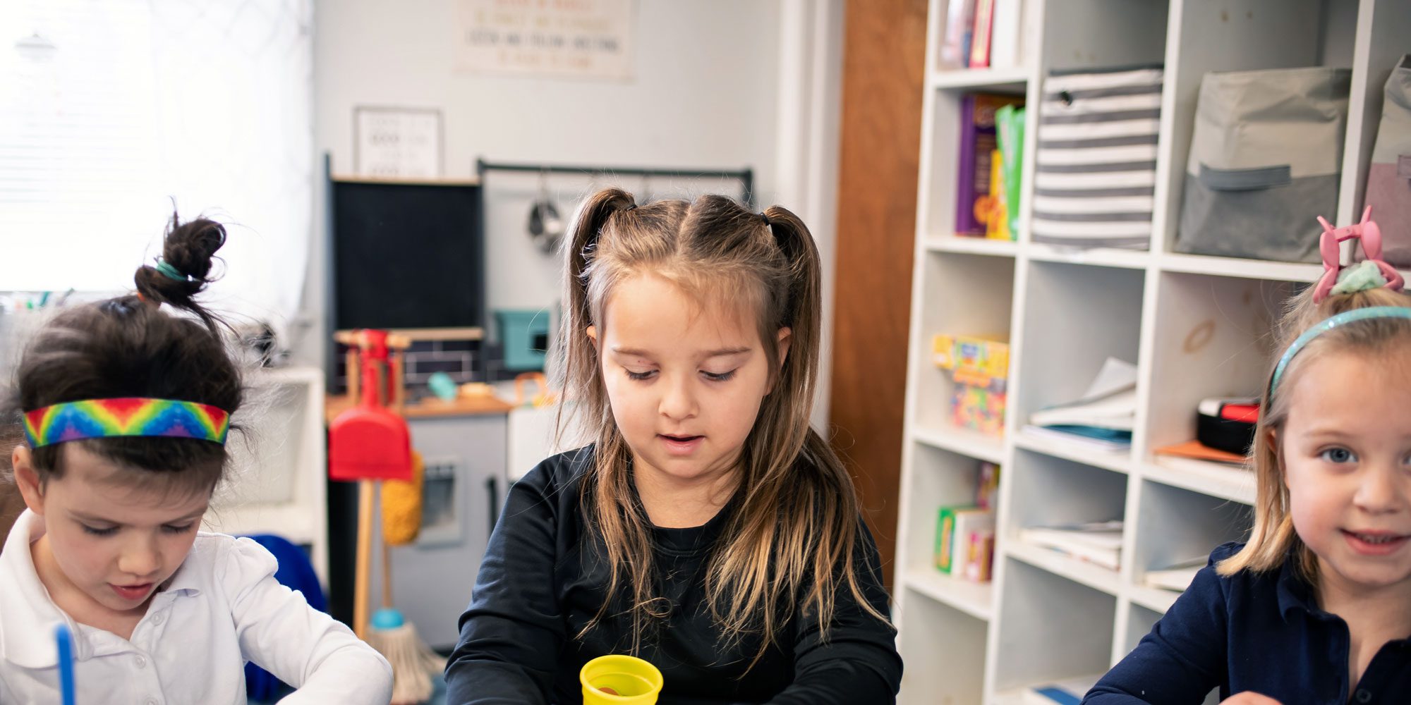 Three young students doing an activity together at a classroom table.