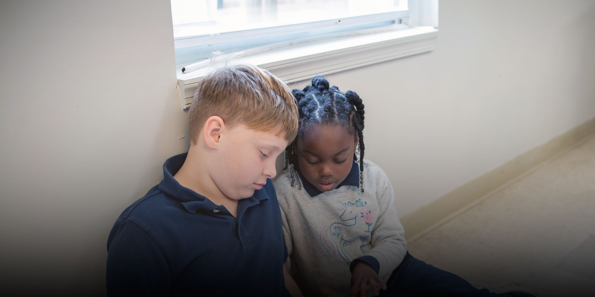 Two students sitting together by a classroom window, working side by side.